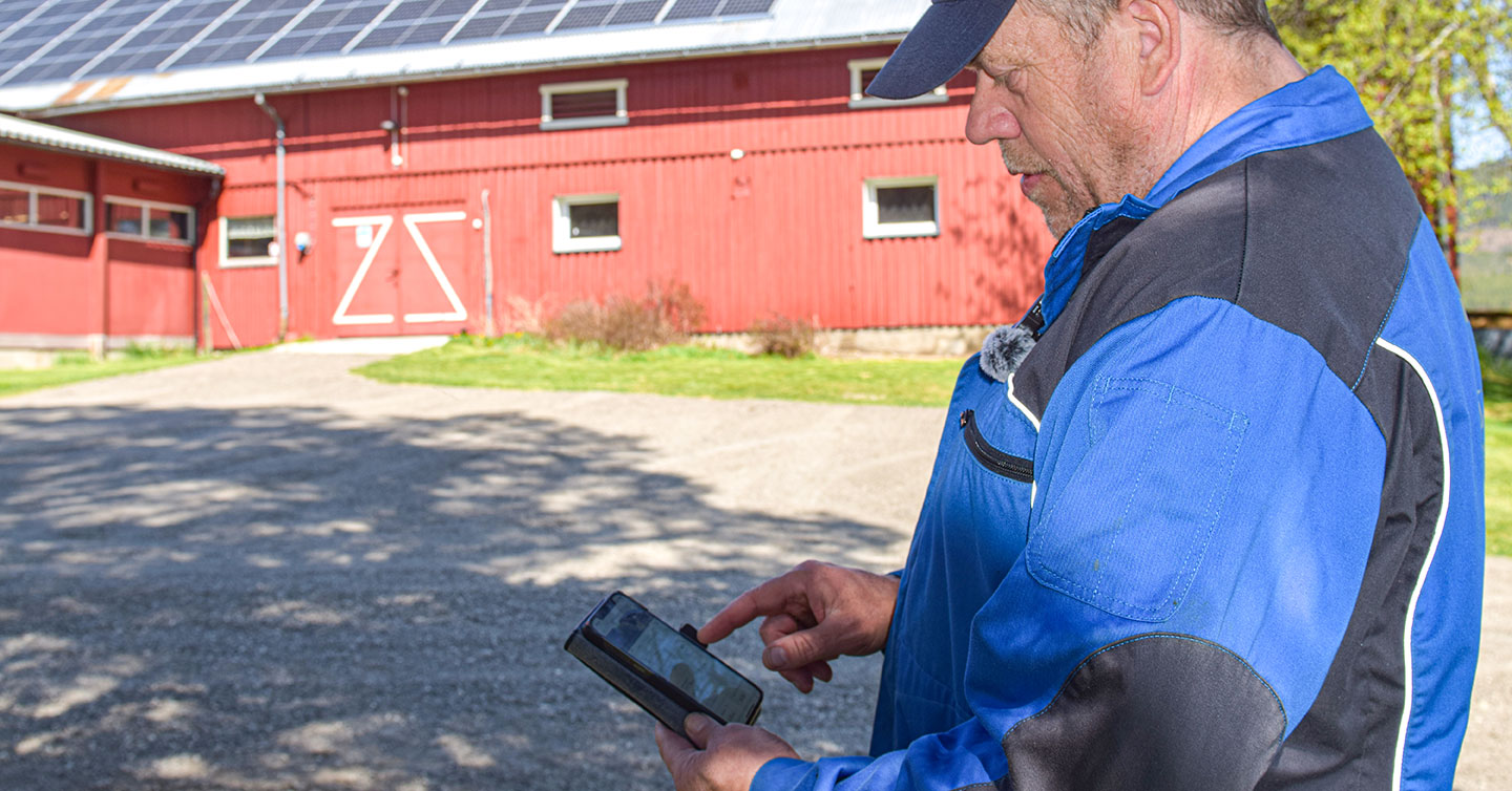 Jon Roger Neslund følger med på solcelleappen for å se hvor mye han produserer, med solcelleanlegget på taket i bakgrunnen